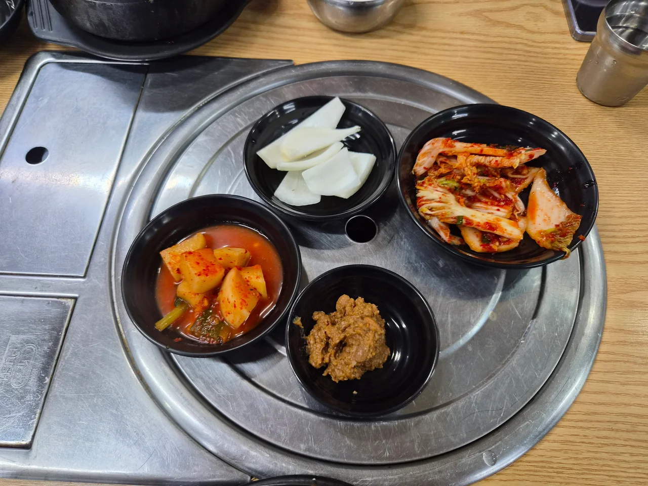 검은 접시에 정갈하게 담긴 겉절이, 깍두기, 양파, 된장 밑반찬